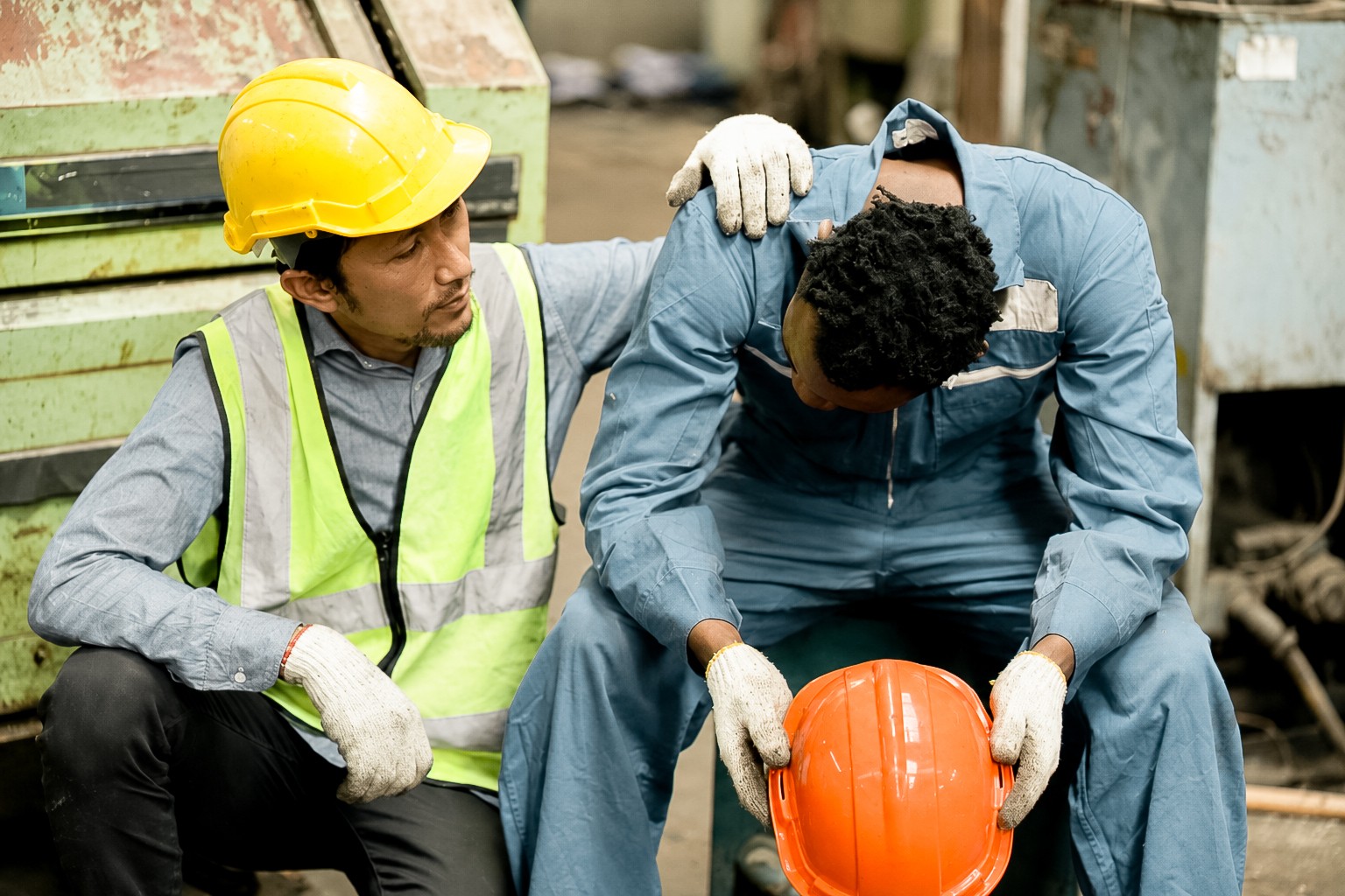 A worker in a hard hat comforting a colleague on a factory floor (stock photo, posed by models)